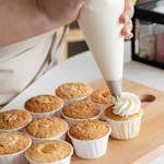 Home 10 High angle of crop unrecognizable confectioner with pastry bag squeezing white cream on cupcakes